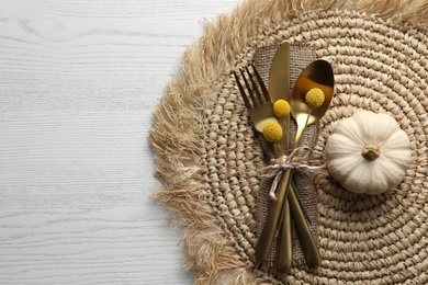 Autumn table setting, space for text. Cutlery with pumpkin and wicker mat on white wooden background, flat lay
