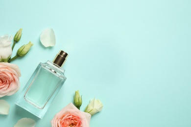 Flat lay composition with bottle of perfume and flowers on cyan background, space for text