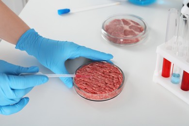 Scientist dripping sample onto raw minced cultured meat at table in laboratory, closeup