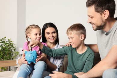 Happy family putting money into piggy bank at home
