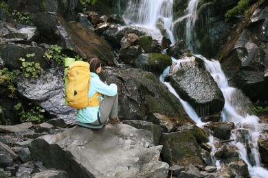 Tourist with yellow backpack enjoying mountain waterfall