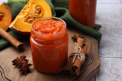 Jar of delicious pumpkin jam and ingredients on tiled surface, closeup