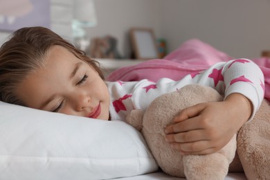 Cute little girl with toy bear sleeping in bed at home