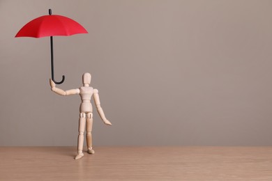 Mannequin holding small umbrella on wooden table. Space for text