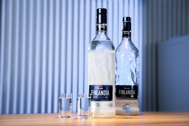 Photo of MYKOLAIV, UKRAINE - SEPTEMBER 23, 2019: Finlandia vodka and shot glasses on wooden bar counter. Space for text