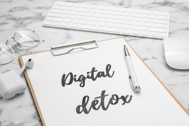 Clipboard with phrase DIGITAL DETOX, earphones and pen on white marble table, closeup