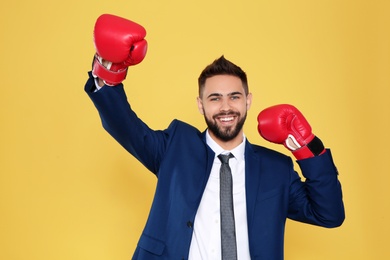 Happy young businessman with boxing gloves celebrating victory on color background