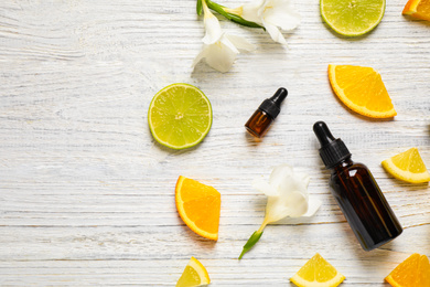 Flat lay composition with bottles of citrus essential oil on white wooden background. Space for text