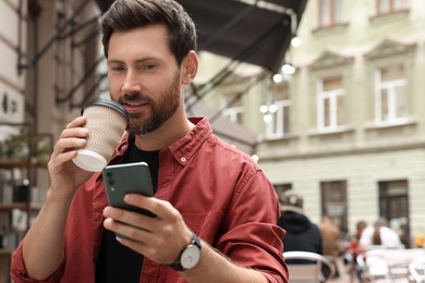 Photo of Handsome man with cup of coffee using smartphone outdoors, space for text