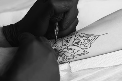 Image of Professional artist making tattoo on hand at table, closeup. Black and white photography
