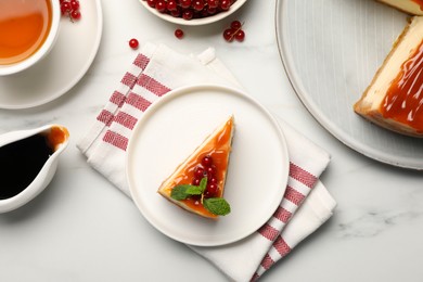 Photo of Piece of delicious caramel cheesecake with red currants and mint served on white marble table, flat lay