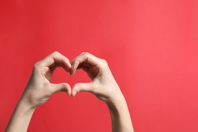 Woman making heart with her hands on red background, closeup. Space for text