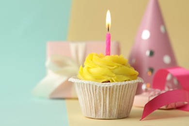 Tasty birthday cupcake with candle, gift box and party hat on colorful background. Space for text