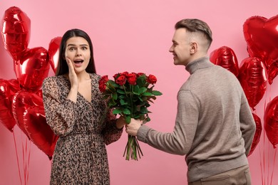 Photo of Boyfriend presenting bouquet of red roses to his girlfriend on pink background. Valentine's day celebration