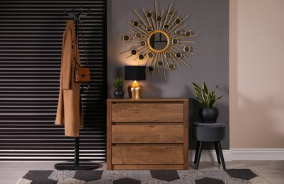 Wooden chest of drawers with decor, coat stand and mirror in hallway. Interior design