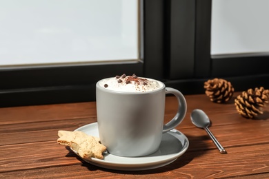 Cup of cappuccino with cookies on windowsill indoors. Winter drink