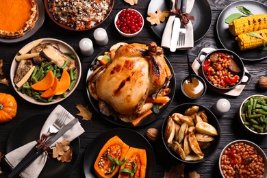 Traditional Thanksgiving day feast with delicious cooked turkey and other seasonal dishes served on black wooden table, flat lay