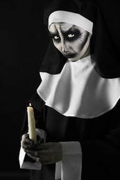 Scary devilish nun with burning candle on black background. Halloween party look