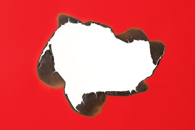 Burnt hole in red paper on white background, space for text