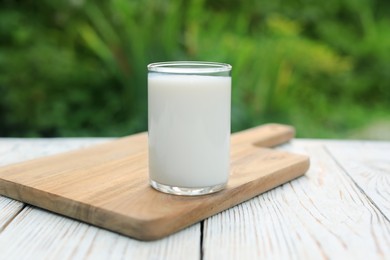 Glass of tasty fresh milk on white wooden table outdoors