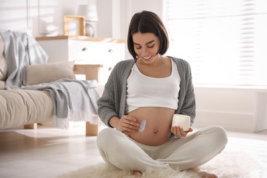 Young pregnant woman with cosmetic product at home