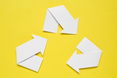 Recycling symbol made of white paper arrows on yellow background, top view