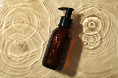 Bottle of hydrophilic oil in water on beige background, top view