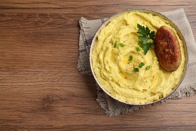 Photo of Bowl of tasty mashed potatoes with parsley, black pepper and cutlet served on wooden table, top view. Space for text