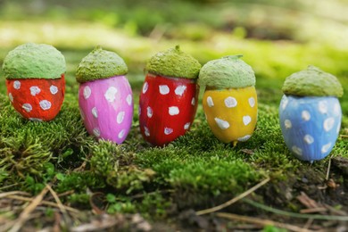 Colorful painted acorns with polka dot pattern on green moss outdoors, closeup