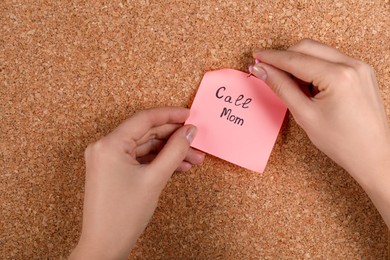 Photo of Woman pinning paper note with phrase Call Mom to cork board, closeup
