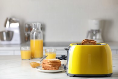 Yellow toaster with roasted bread slices, jam, juice and blueberries on white marble table