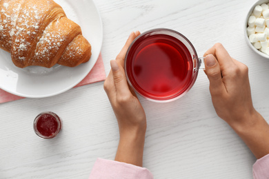 Woman holding glass cup of raspberry tea at white wooden table, top view. Delicious morning meal