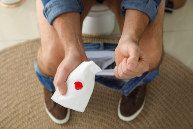 Man holding toilet paper with blood stain in rest room, closeup. Hemorrhoid concept
