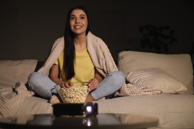 Young woman watching movie with popcorn on sofa at night