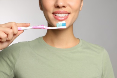 Woman holding toothbrush with paste on light background, closeup