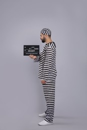 Prisoner in special uniform with mugshot letter board  
on grey background