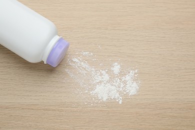 Photo of Bottle and scattered dusting powder on wooden background, top view. Baby cosmetic product