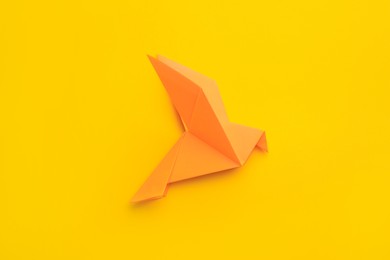 Photo of Origami art. Beautiful handmade paper bird on yellow background, top view