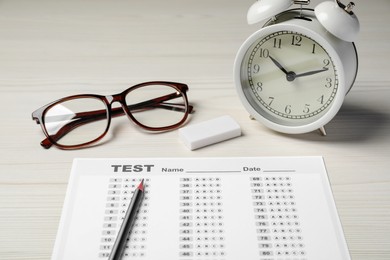 Photo of Composition with answer sheet, alarm clock and eyeglasses on white wooden table. Student passing exam