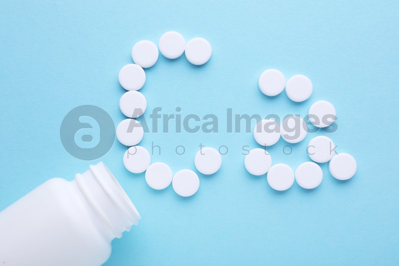 Photo of Open bottle and calcium symbol made of white pills on light blue background, flat lay
