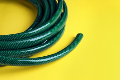 Green rubber watering hose on yellow background, closeup. Space for text