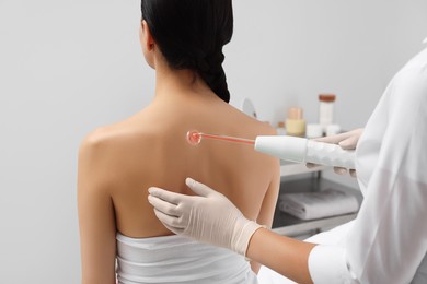 Woman undergoing physiotherapy procedure with darsonval in salon, back view
