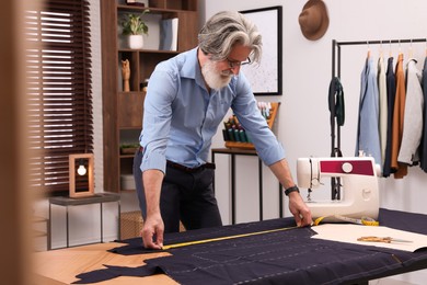Professional tailor with measuring tape working at table in atelier