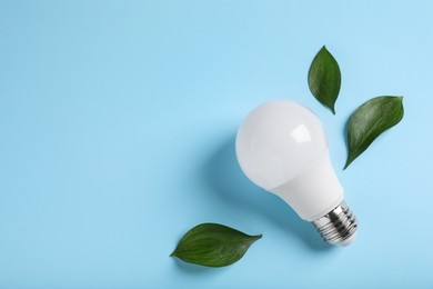 Light bulb and green leaves on color background, flat lay. Space for text