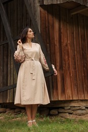 Beautiful woman wearing embroidered dress near old wooden mill in countryside. Ukrainian national clothes