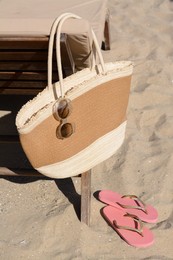 Straw bag with sunglasses and flip flops on sand . Beach accessories