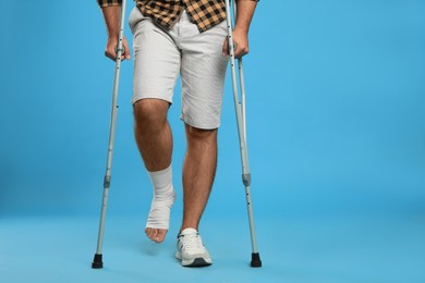 Young man with injured leg using axillary crutches on light blue background, closeup