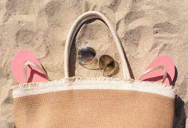 Photo of Pink flip flops, sunglasses and straw bag on sand, flat lay. Beach accessories