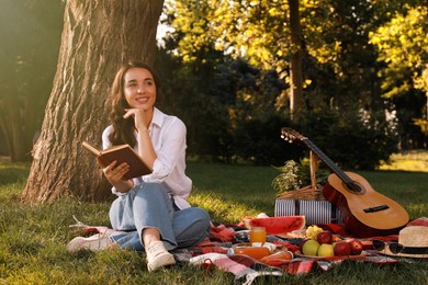 Happy young woman reading book on plaid in park. Summer picnic