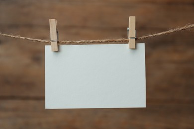 Clothespins with blank notepaper on twine against wooden background. Space for text